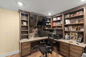 Office with built in study area, wood finished floors, visible vents, and baseboards
