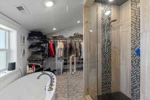 Full bath with lofted ceiling, a spacious closet, visible vents, a bath, and a stall shower