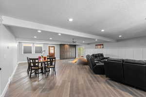 Living room with wood finished floors, a ceiling fan, beam ceiling, baseboards, and a textured ceiling