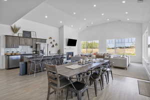 Dining space with light wood finished floors, a glass covered fireplace, high vaulted ceiling, and recessed lighting