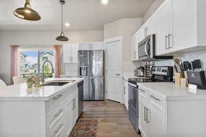 Kitchen with white cabinets, light countertops, backsplash, a sink, and appliances with stainless steel finishes
