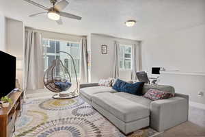 Carpeted living area with a textured ceiling, a healthy amount of sunlight, a ceiling fan, and baseboards