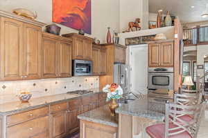 Kitchen featuring stainless steel appliances, a sink, tasteful backsplash, light stone counters, and a breakfast bar area