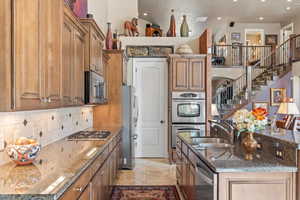 Kitchen featuring an island with sink, stainless steel appliances, a sink, dark stone counters, and decorative backsplash