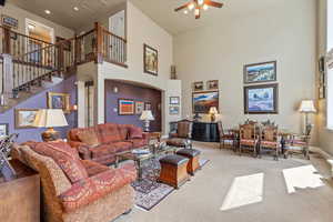 Living area with carpet, a towering ceiling, a ceiling fan, arched walkways, and stairs