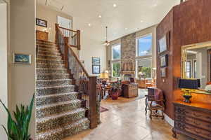 Staircase featuring a towering ceiling, recessed lighting, a ceiling fan, a large fireplace, and tile patterned flooring