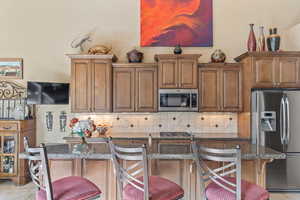 Kitchen featuring tasteful backsplash, dark stone countertops, stainless steel appliances, and a breakfast bar