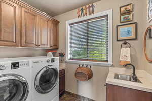 Clothes washing area featuring a sink, washing machine and dryer, baseboards, cabinet space, and dark tile patterned flooring