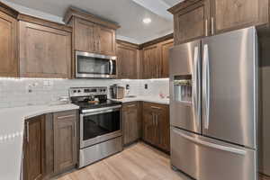 Kitchen with tasteful backsplash, stainless steel appliances, light countertops, and light wood-style floors
