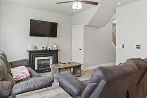 Living area featuring stairway, wood finished floors, ceiling fan, a premium fireplace, and baseboards