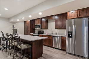 Kitchen with stainless steel appliances, light wood-style flooring, a sink, recessed lighting, and a breakfast bar