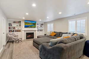 Living area with recessed lighting, a warm lit fireplace, visible vents, light wood-type flooring, and built in features