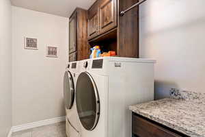 Laundry room with cabinet space, washing machine and clothes dryer, baseboards, and light tile patterned floors