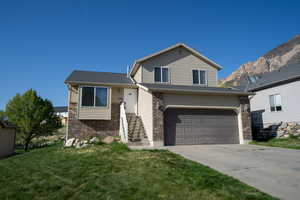 Tri-level home featuring a front lawn, driveway, brick siding, a mountain view, and a garage