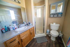 Full bathroom with a shower stall, toilet, vanity, and wood finished floors