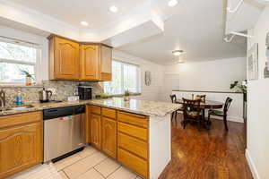 Kitchen featuring a peninsula, stainless steel dishwasher, a sink, light stone counters, and crown molding