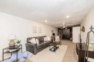 Carpeted living room with a ceiling fan, a textured ceiling, and recessed lighting