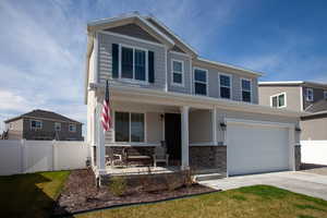View of front of home with a porch, fence, stone siding, Jelly Fish Lighting and concrete driveway