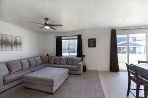 Living area with plenty of natural light, a ceiling fan, and light colored carpet.