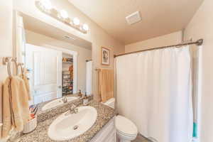 Full bath with visible vents, toilet, vanity, and a textured ceiling