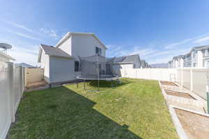 Back of house featuring a yard, a fenced backyard, a vegetable garden, and a trampoline