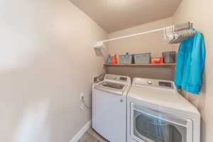 Clothes washing area with washer and dryer, laundry area, baseboards, and a textured ceiling