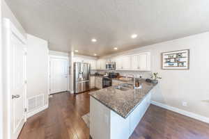 Kitchen with baseboards, a peninsula, visible vents, appliances with stainless steel finishes, and a sink