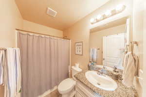 Full bath with toilet, curtained shower, vanity, and visible vents