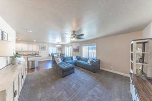 Living area featuring dark colored carpet, a textured ceiling, baseboards, and ceiling fan