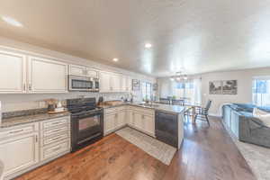 Kitchen with a sink, open floor plan, a peninsula, a textured ceiling, and black appliances