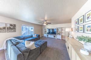 Living area featuring dark carpet, baseboards, a ceiling fan, and a textured ceiling