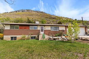 Ranch-style home featuring a mountain view, driveway, a garage, brick siding, and a front yard