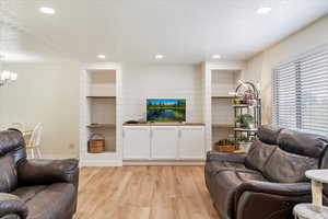 Living area with light wood style laminate  floors, and recessed lighting