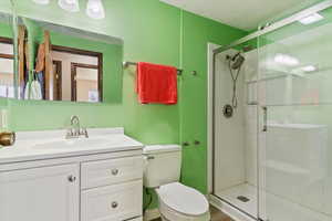 Bathroom featuring a shower stall, a textured wall, toilet, and vanity