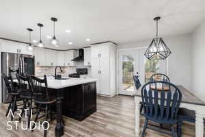 Kitchen featuring a sink, light wood-style floors, stove, wall chimney range hood, and stainless steel refrigerator with ice dispenser