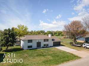 View of front of home with an attached garage, a chimney, a front yard, and concrete driveway