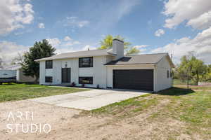 Raised ranch featuring a front lawn, driveway, a chimney, brick siding, and an attached garage
