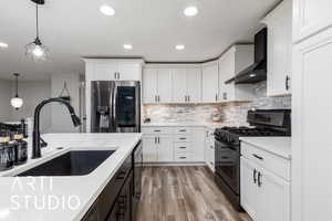 Kitchen featuring light countertops, a sink, wall chimney exhaust hood, pendant lighting, and black appliances