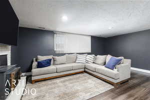 Living room with wood finished floors, visible vents, baseboards, a fireplace, and a textured ceiling