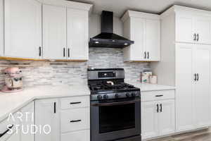 Kitchen with wall chimney exhaust hood, stainless steel range with gas stovetop, light countertops, and white cabinetry