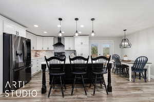 Kitchen featuring a kitchen breakfast bar, stainless steel fridge with ice dispenser, white cabinets, wall chimney exhaust hood, and stove