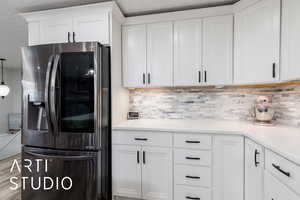 Kitchen with white cabinets, stainless steel fridge with ice dispenser, decorative backsplash, and light countertops
