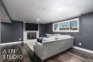 Living room with wood finished floors, a brick fireplace, baseboards, and a textured ceiling