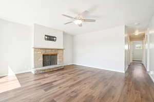 Unfurnished living room featuring a fireplace, wood finished floors, baseboards, and ceiling fan