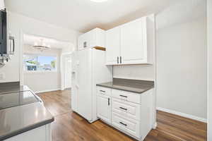 Kitchen featuring stainless steel microwave, dark wood-style flooring, dark countertops, white cabinetry, and white refrigerator with ice dispenser