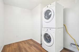 Laundry area featuring stacked washing maching and dryer, baseboards, wood finished floors, and laundry area