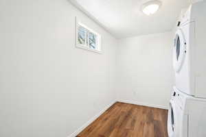 Laundry room with stacked washer / dryer, laundry area, wood finished floors, baseboards, and a textured ceiling