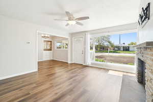 Unfurnished living room with baseboards, wood finished floors, ceiling fan with notable chandelier, and a fireplace