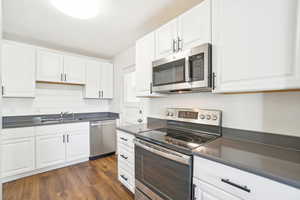 Kitchen with white cabinets, dark wood finished floors, dark countertops, a sink, and appliances with stainless steel finishes