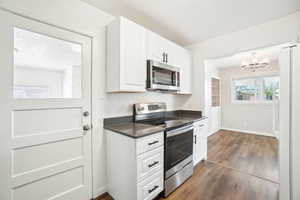 Kitchen with stainless steel appliances, dark wood-style flooring, dark countertops, a chandelier, and white cabinetry